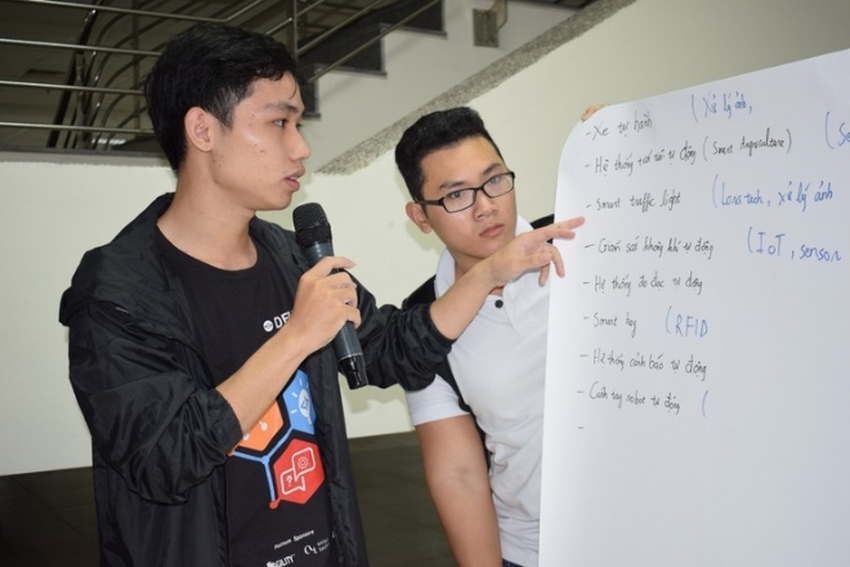 A person speaking into a microphone next to a person writing on a whiteboard

Description automatically generated with medium confidence