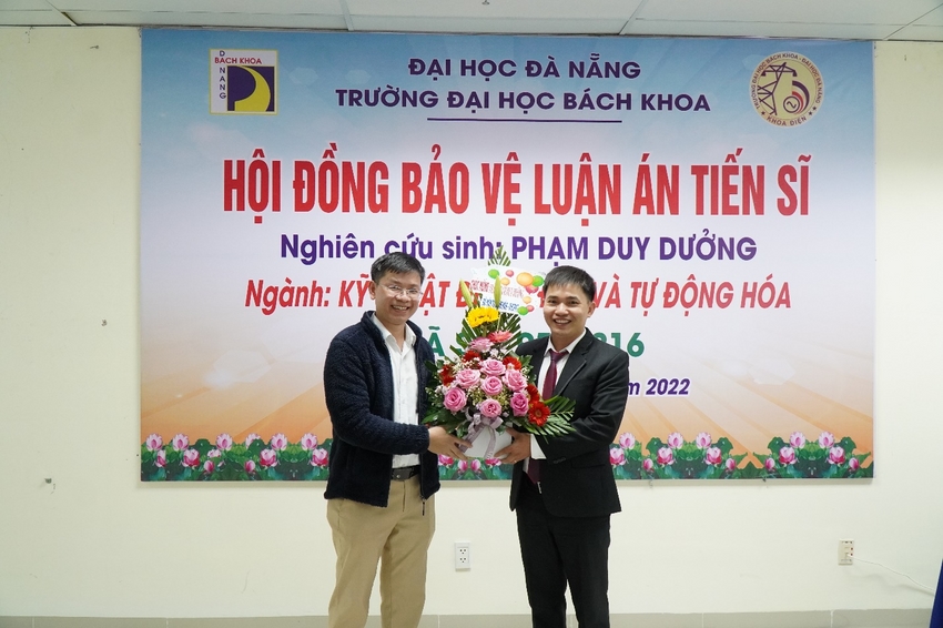 A couple of men standing in front of a sign
Description automatically generated with low confidence