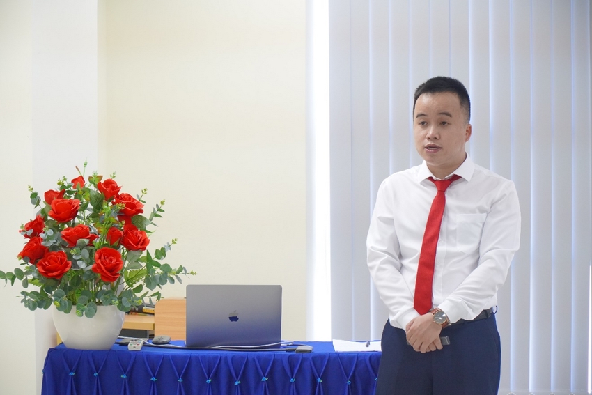 A person standing in front of a table with a computer and flowers

Description automatically generated