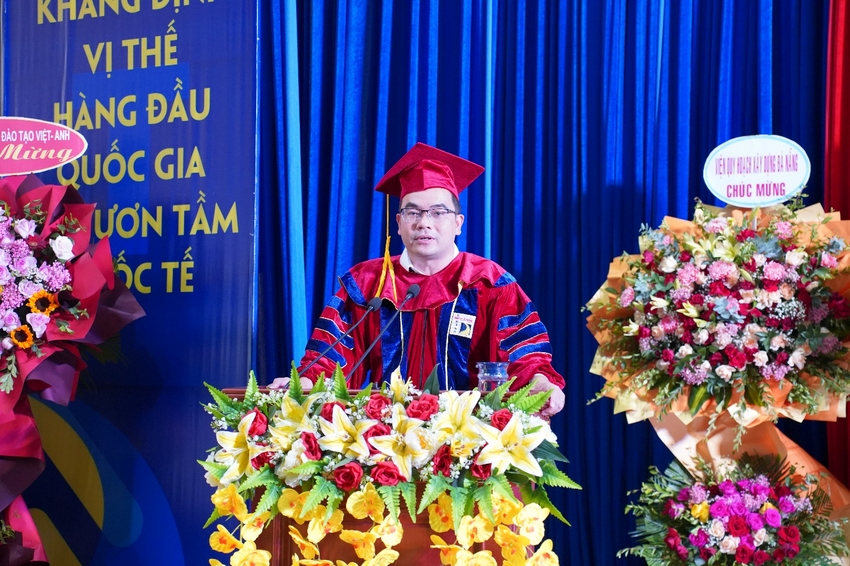 A person in a graduation gown and cap standing at a podium with flowers

Description automatically generated