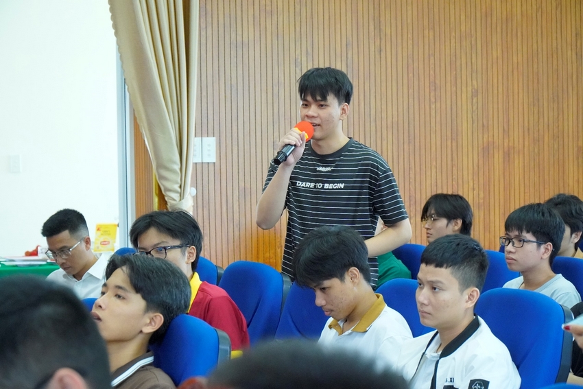 A person speaking into a microphone in front of a group of people

Description automatically generated