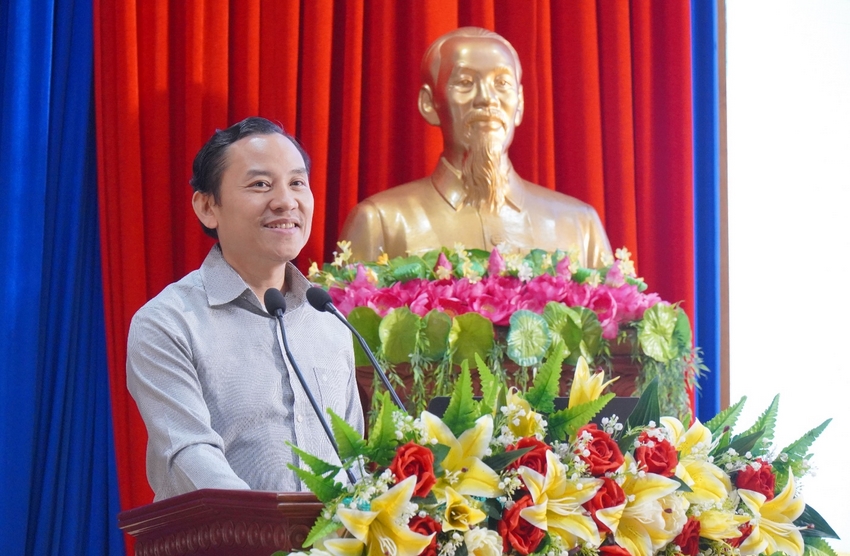 A person standing at a podium with a microphone and flowers

Description automatically generated