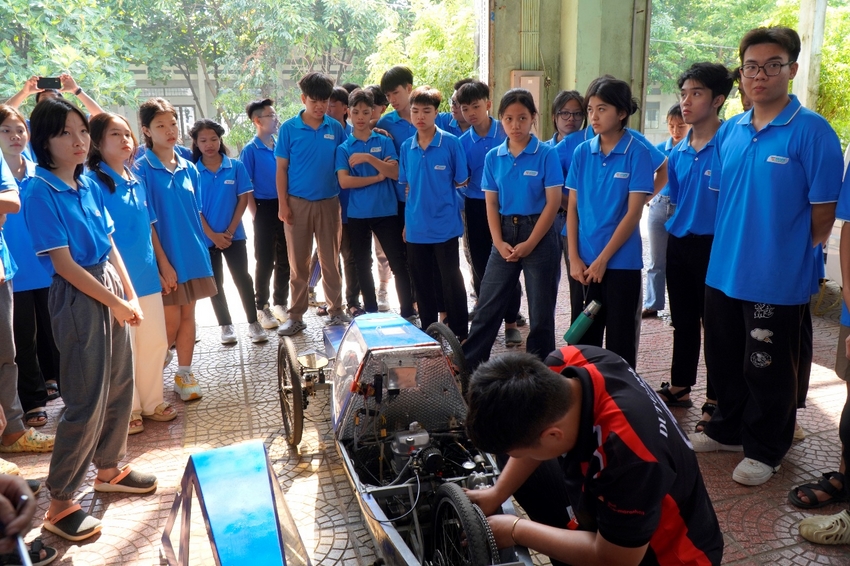 A group of people in blue shirts standing around a small vehicle

Description automatically generated